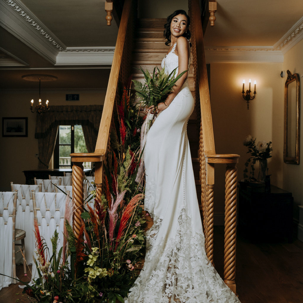 Bride in Lace Wedding Dress Holding Flowers on a Staircase
