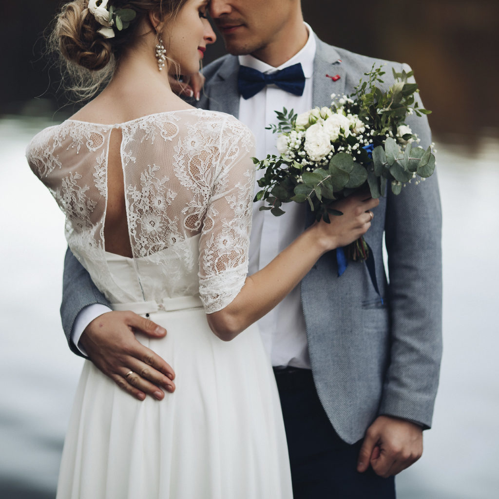 Newlywed Couple in an Embrace with Pretty White Bouquet of Flowers