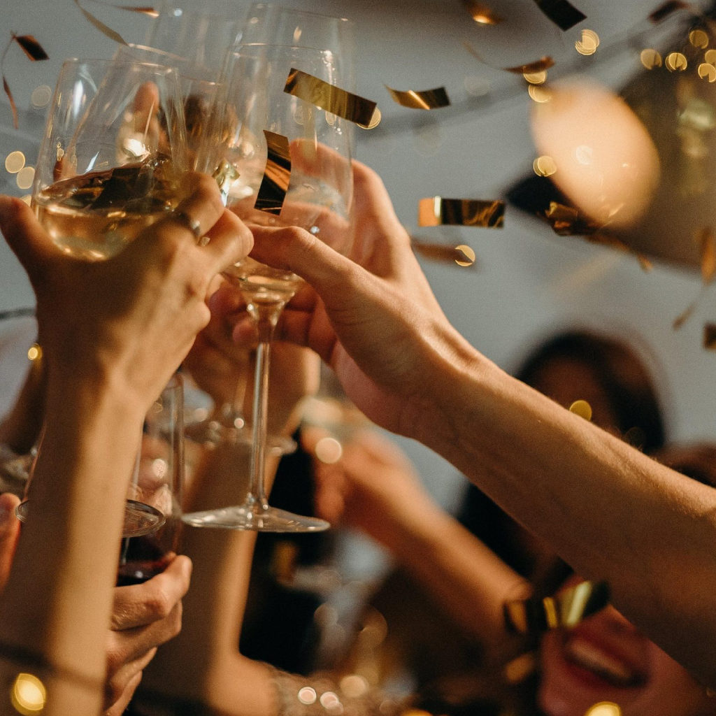 People At A Party Clinking Glasses of Champagne in the Air with Confetti
