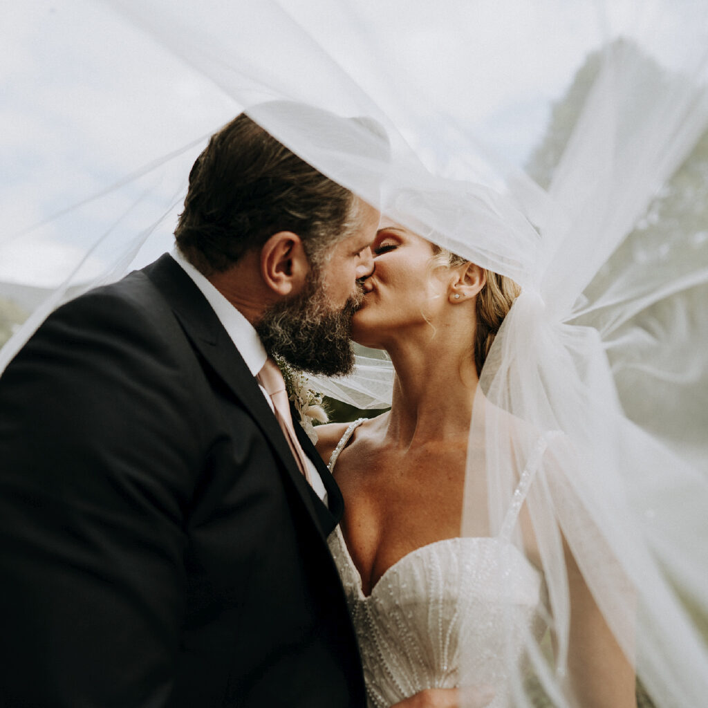 Bride and groom kissing beneath brides veil
