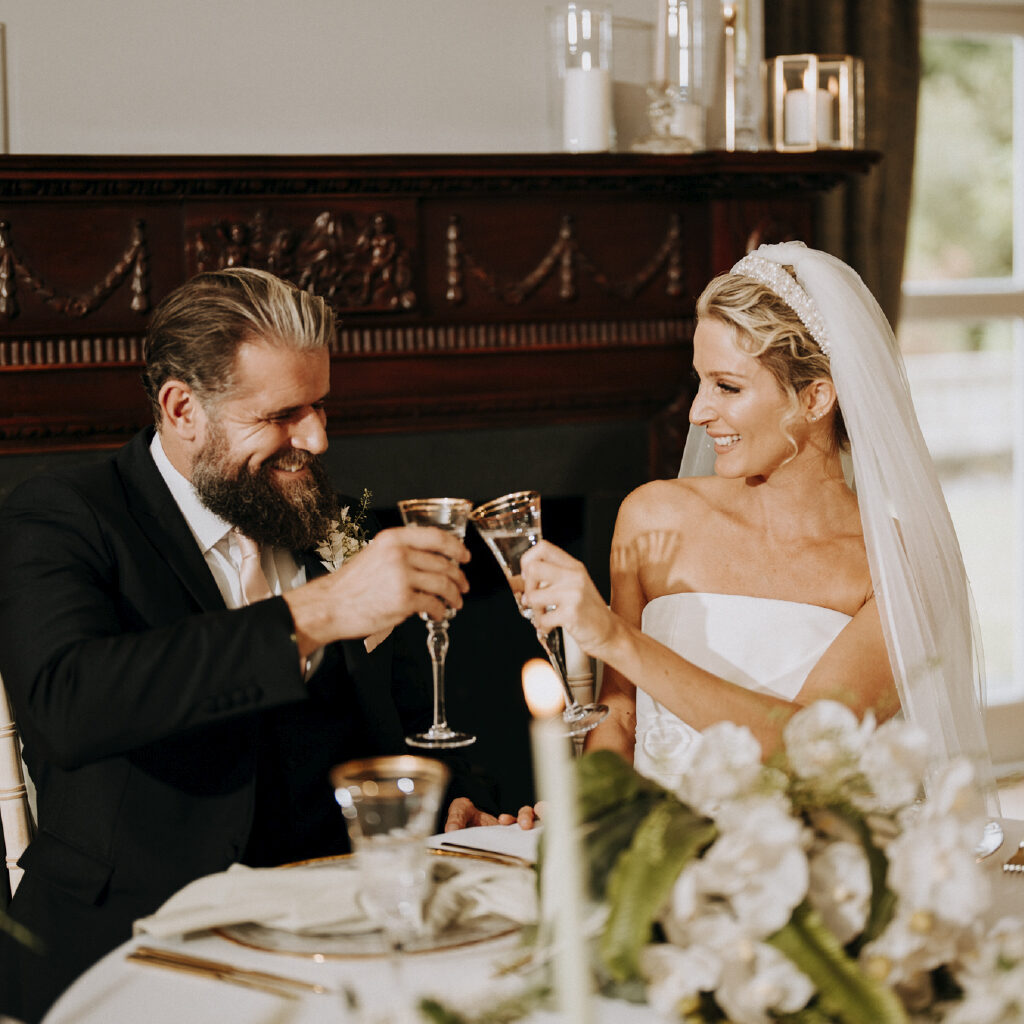Bride and groom laughing and clinking glasses around the sweetheart table