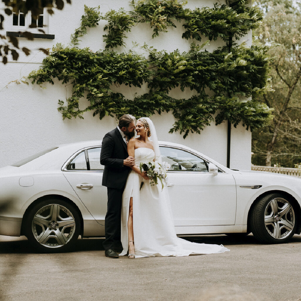 Bride and groom stood in front of a white Bentley