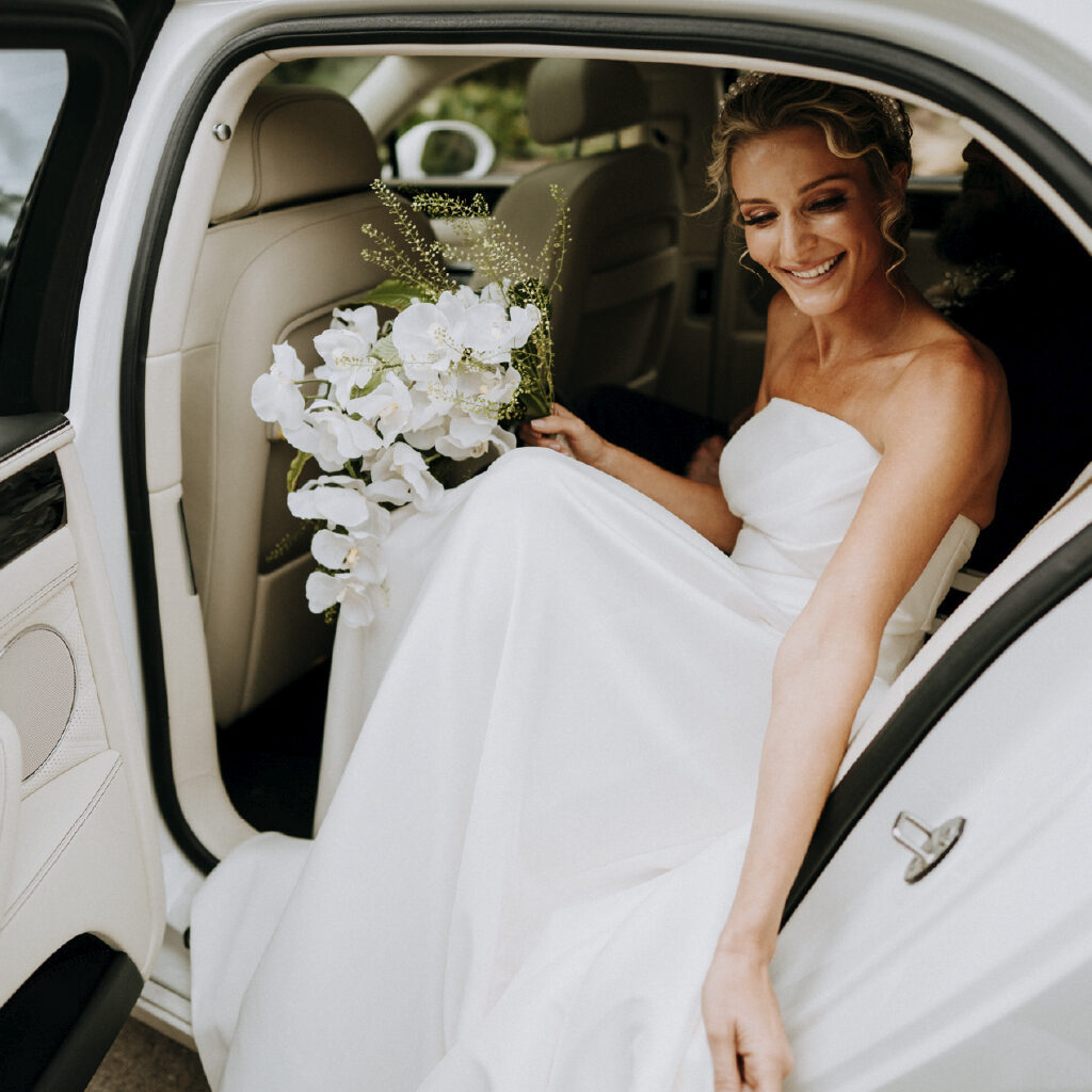 Close up of beautiful bride with white lily bouquet getting out of a white bridal car